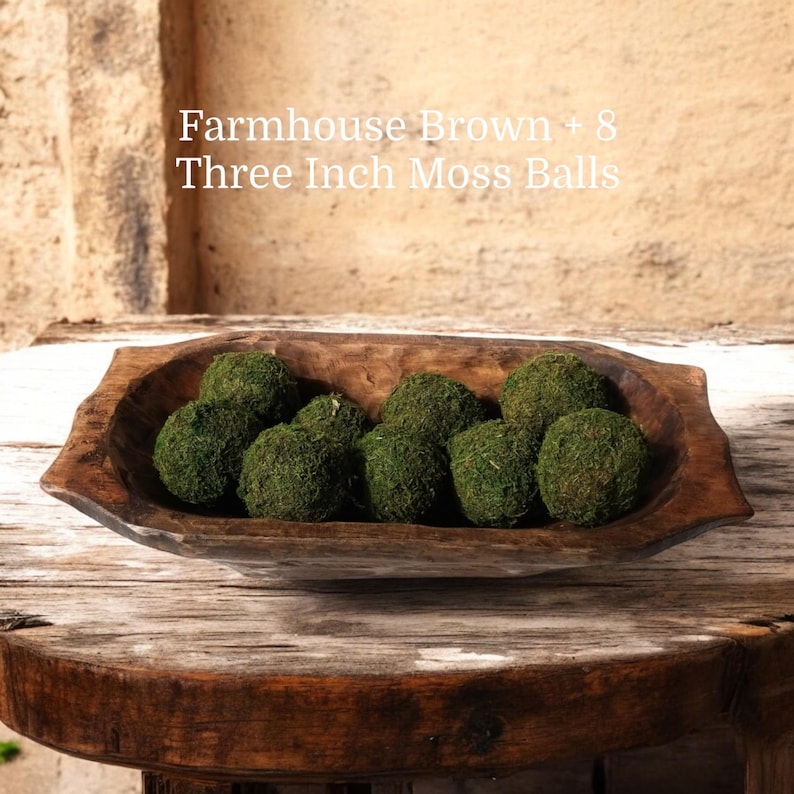 May include: A wooden bowl filled with eight green moss balls. The bowl is brown and has a rustic look. The text "Farmhouse Brown + 8 Three Inch Moss Balls" is written above the bowl.