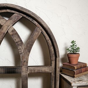 May include: A rustic, arched wooden wall decor with a distressed finish. A small potted succulent sits atop a stack of vintage books on a wooden side table. The decor has a farmhouse style.