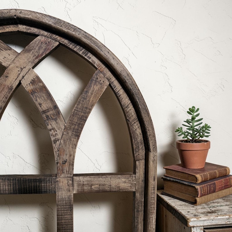 May include: A rustic, arched wooden wall decor with a distressed finish. A small potted succulent sits atop a stack of vintage books on a wooden side table. The decor has a farmhouse style.