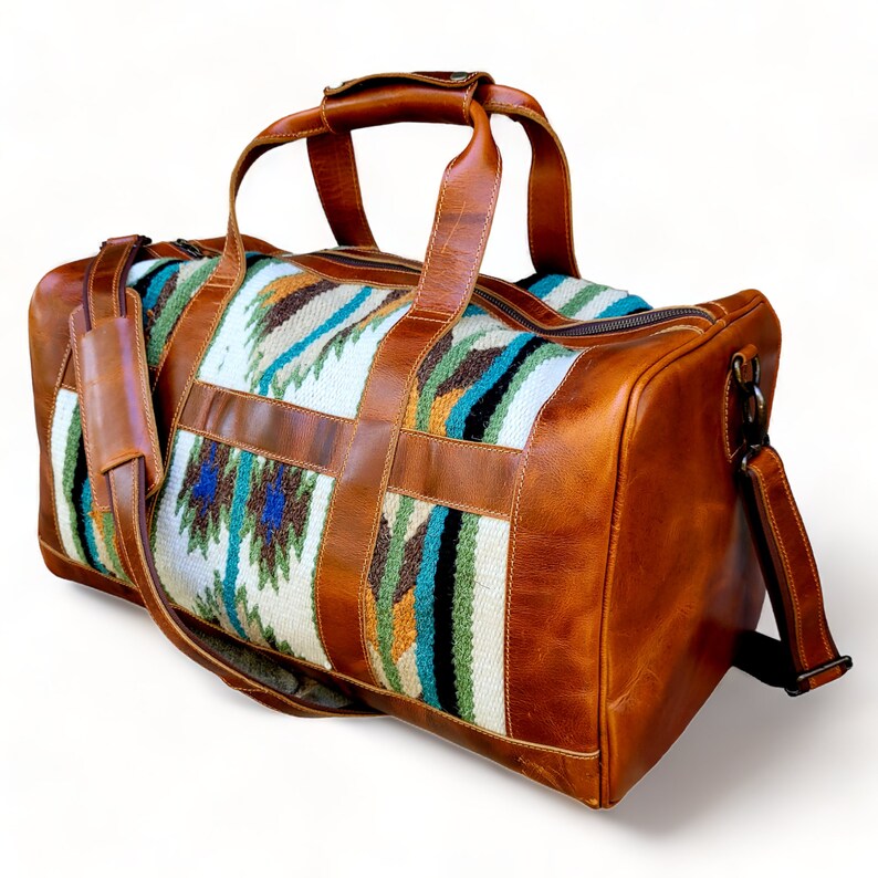 May include: A brown leather duffel bag with a woven pattern in shades of white, blue, green, and orange. The bag has a top handle and a shoulder strap.