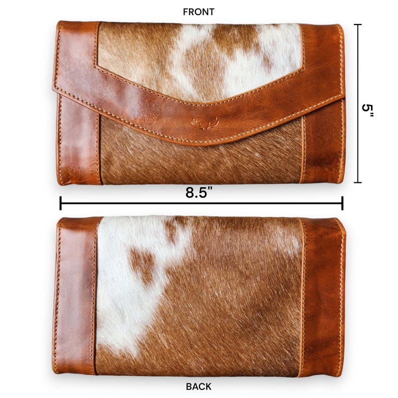 Op de afbeelding: Een bruin en witte koeienhuid portemonnee met een leren flap en afwerking. De portemonnee is 21,6 cm lang en 12,7 cm hoog. De voor- en achterkant van de portemonnee worden getoond. De portemonnee heeft een getextureerde uitstraling.
