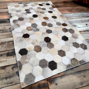 May include: A white, brown, and gray cowhide rug with a hexagonal pattern. The rug is made of individual pieces of cowhide that have been sewn together.
