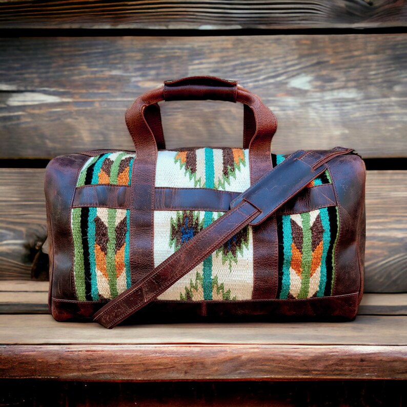 May include: A brown leather duffel bag with a woven pattern in shades of green, orange, and blue. The bag has a long shoulder strap and two top handles.