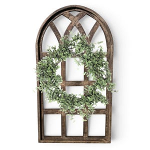 May include: A rustic, arched wooden window frame with a lattice design. A circular green leafy wreath is centered on the frame. The wood has a dark brown finish, and the wreath is a vibrant green, creating a natural, decorative piece.