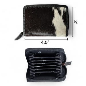 May include: A black and white cowhide leather wallet with a zipper closure. The wallet is 4.5 inches wide and 3 inches tall. The inside of the wallet has multiple card slots.