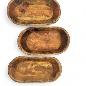 May include: Three wooden dough bowls of varying sizes. The bowls are oval shaped and have a rustic, natural finish.