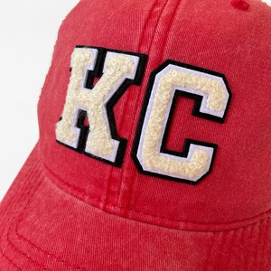 May include: Red baseball cap with a white and black felt "KC" patch on the front.