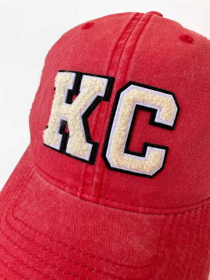 May include: Red baseball cap with a white and black felt "KC" patch on the front.