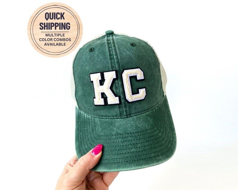 May include: A green and white trucker hat with the letters "KC" embroidered in white on the front.