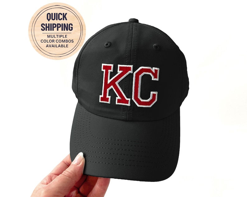 May include: Black baseball cap with the letters "KC" in red with a white outline. The cap has a curved brim and a structured crown. The image also includes a circular sticker with the text "Quick Shipping" and "Multiple Color Combos Available".