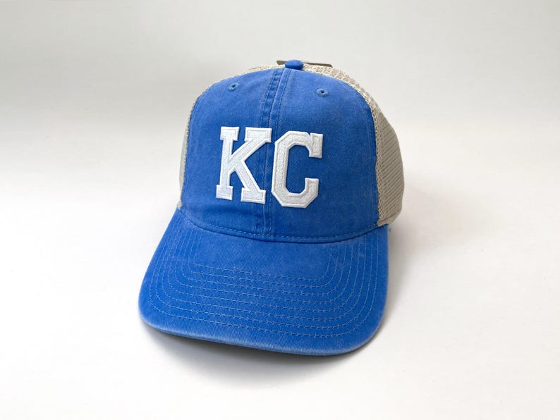 May include: A blue and beige trucker hat with a white embroidered "KC" on the front.