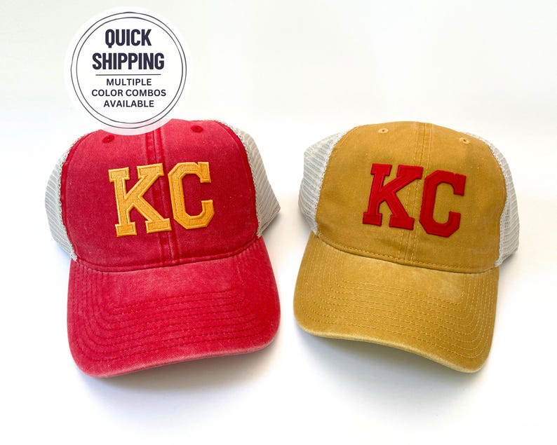 May include: Two trucker hats with a mesh back. One hat is red with a yellow "KC" embroidered on the front. The other hat is yellow with a red "KC" embroidered on the front.