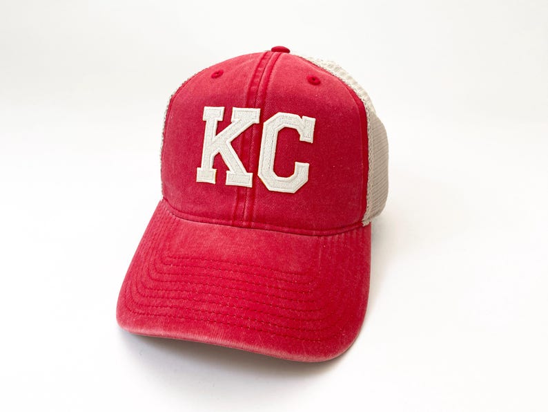 May include: Red and white trucker hat with the letters "KC" embroidered on the front.