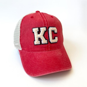 May include: Red and white trucker hat with the letters "KC" in white on the front.