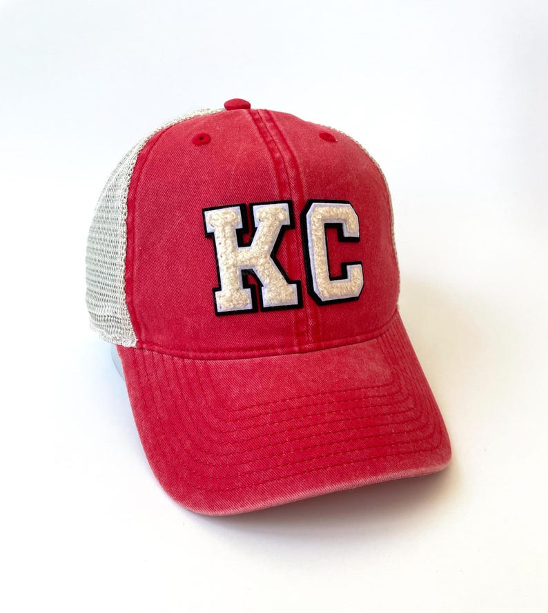 May include: Red and white trucker hat with the letters "KC" in white on the front.