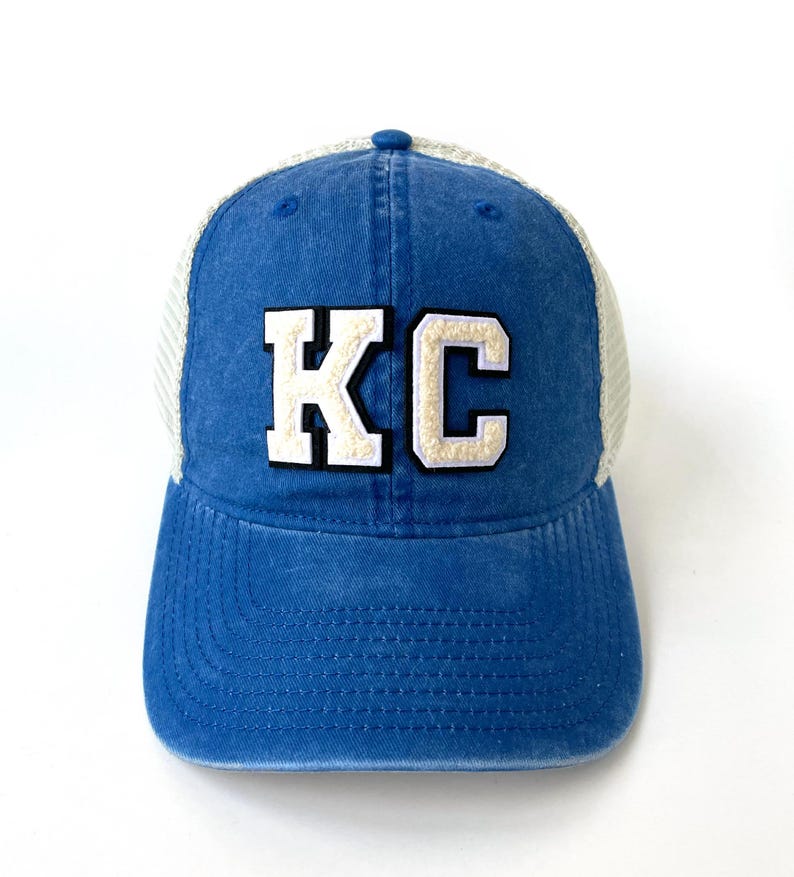 May include: A blue and white trucker hat with a white felt patch that says "KC" in block letters.