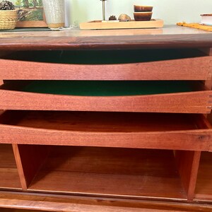 May include: A wooden cabinet with three drawers and open shelves. The drawers are made of a light wood and have a green felt lining. The shelves are made of a darker wood.