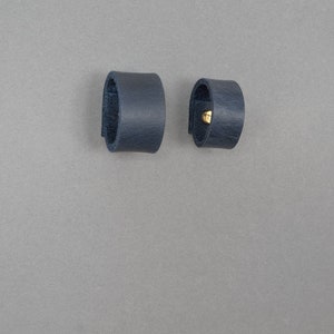 May include: Two dark blue leather rings, one with a gold metal accent.