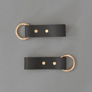 May include: Two black leather straps with gold metal rings and brass rivets. Each strap has two brass rivets.