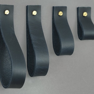 May include: Four black leather drawer pulls with brass screws. The pulls are different sizes and are arranged in order from largest to smallest.