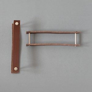 May include: Two brown leather straps with silver metal rivets. One strap is straight and the other is curved into a U-shape.