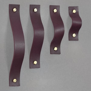 Puede incluir: Cinco tiradores de armario de cuero burdeos con un diseño ondulado y tornillos dorados.