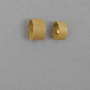 May include: Two brown leather cuff bracelets. One bracelet has a small gold screw detail.