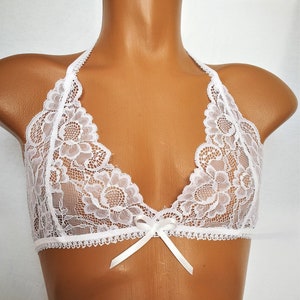 Op de afbeelding: Witte kanten bralette met halternek en een strik in het midden. De bralette is gemaakt van delicate kant en heeft een gegolfde rand.