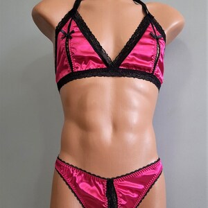 May include: A pink satin lingerie set with black lace trim. The bra has a triangle shape and the panties are a thong style.