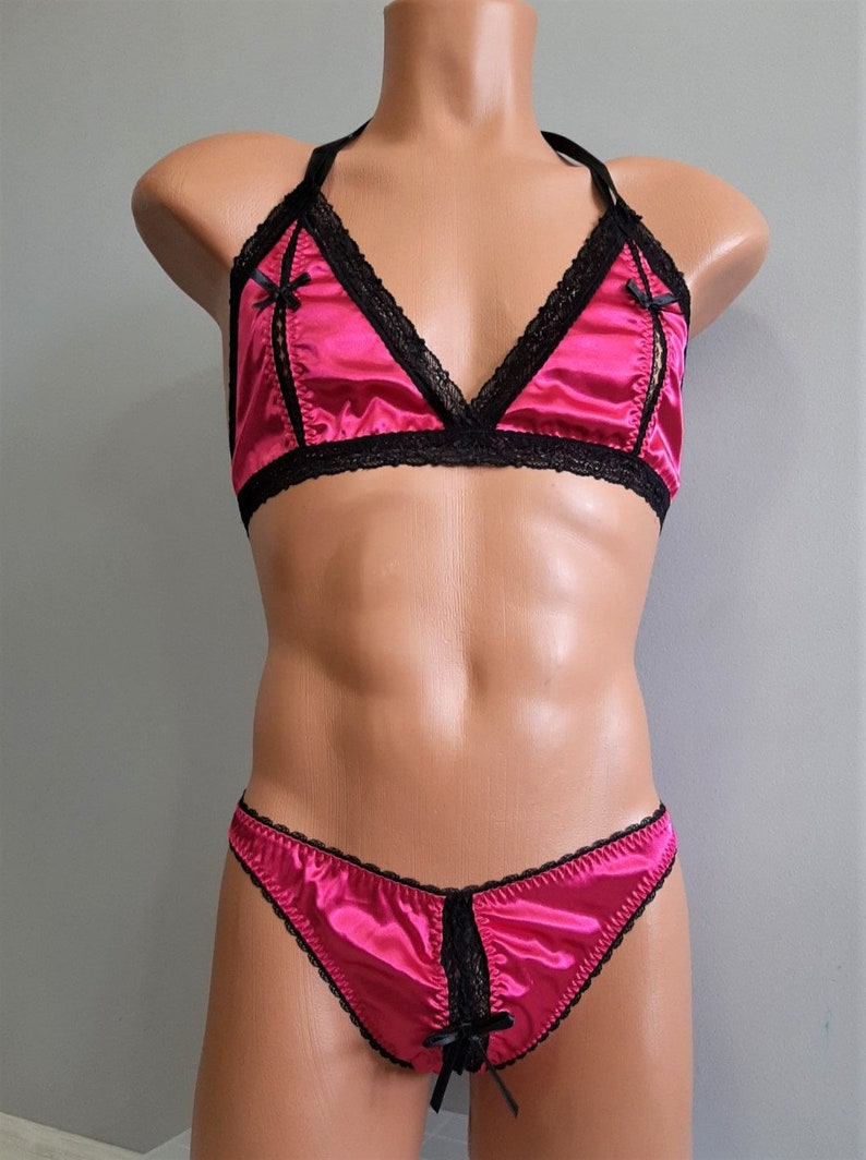 May include: A pink satin lingerie set with black lace trim. The bra has a triangle shape and the panties are a thong style.