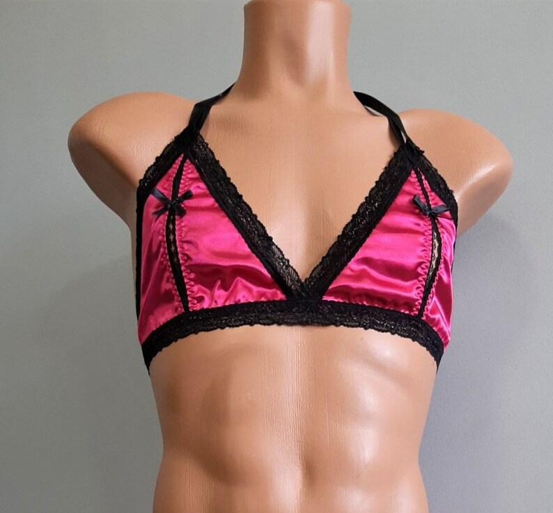 May include: A pink satin triangle bra with black lace trim and black satin bows on the straps.