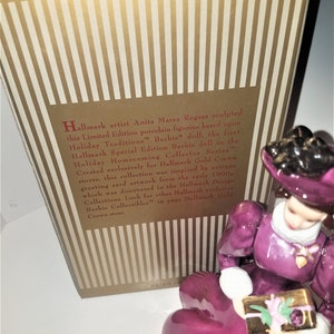 May include: A porcelain figurine of a woman in a purple dress holding a gift box. The figurine is based on the first Hallmark Special Edition Barbie doll in the Holiday Homecoming Collector Series. Hallmark artist Anita Marra Rogers sculpted this figurine.
