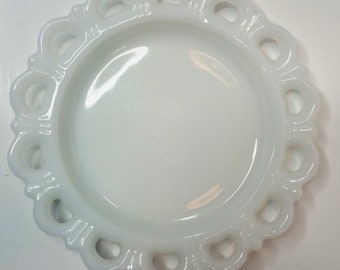 May include: White milk glass plate with a scalloped edge and openwork design. The plate is round and has a smooth, glossy finish.