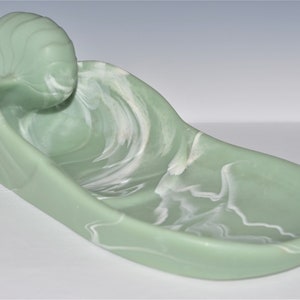 May include: A green ceramic dish with white marbling, shaped like a seashell. The dish is designed to hold small items, such as jewelry or trinkets.