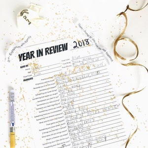May include: A printable year in review worksheet with a black and white design. The worksheet includes questions about favorite color, book, activity, and highlights of the year. The worksheet is decorated with gold glitter.