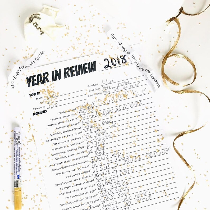May include: A printable year in review worksheet with a black and white design. The worksheet includes questions about favorite color, book, activity, and highlights of the year. The worksheet is decorated with gold glitter.