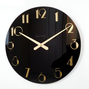 May include: A black round clock with gold Roman numeral hour markers and gold hands. The clock face has the text "Rocco Verre" printed on it.