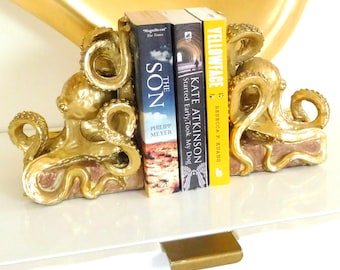 Könnte beinhalten: Goldene Tintenfisch-Buchstützen, die drei Bücher halten. Die Buchtitel lauten "The Son" von Philipp Meyer, "Started Early Took My Dog" von Kate Atkinson und "Yellowface" von Rebecca F. Kuang.