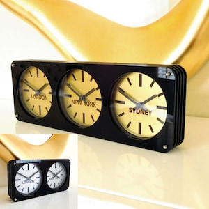 May include: Black rectangular clock with three round faces displaying the time in London, New York, and Sydney. Each face has black hands and black numbers on a yellow background.