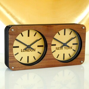 May include: A wooden clock with two faces, one showing the time in London and the other showing the time in New York.