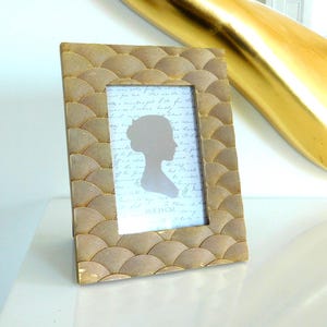 May include: A gold-coloured picture frame featuring a fan-like design. The frame displays a picture with a woman's silhouette and handwritten text. The frame is labelled "10 x 15 cm".