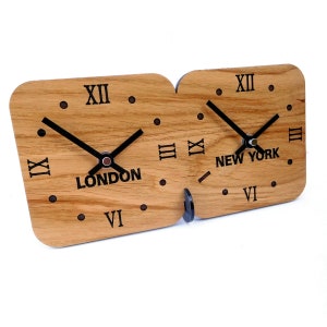 May include: A wooden clock with two faces, one showing the time in London and the other showing the time in New York. The clock is made of light brown wood with black Roman numeral markings and black hands.