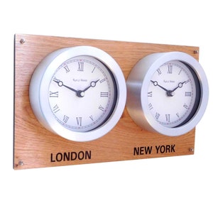 May include: A wooden wall clock with two silver-toned clock faces. The clock faces have Roman numeral markings and the words "Rocco Vendet" printed on them. The clock faces are labeled "London" and "New York".