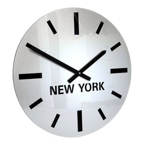 May include: A white round clock with black hour and minute hands and black Roman numeral markings. The clock face has the words "NEW YORK" printed in black.