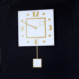 May include: A white square clock with gold Roman numerals and a gold pendulum. The clock face has a gold frame and the hands are gold.