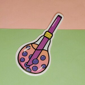May include: A sticker featuring a cartoon illustration of a boba tea drink. The drink is in a clear, bulb-shaped container with a purple straw. The drink itself is pink with purple boba pearls. The straw is purple with a yellow band.