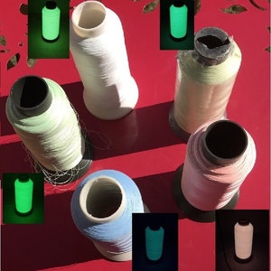 May include: A collection of colorful spools of thread, including white, light green, pink, and blue. Several smaller images show the thread glowing green in the dark. The spools are on a red surface.