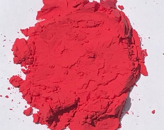 May include: A pile of bright red powder on a white surface. The powder is finely ground and has a smooth texture.