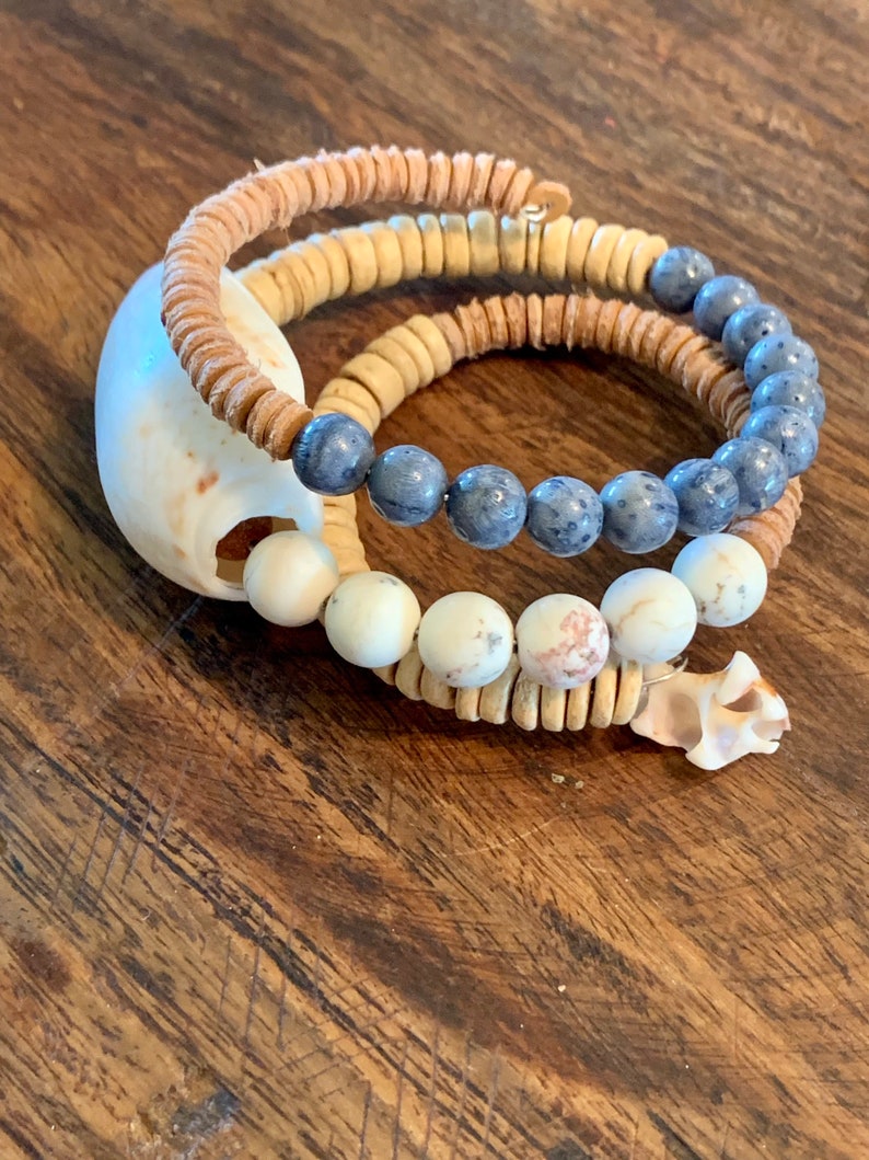 Pu&ograve; includere: Tre braccialetti sovrapposti con perline blu, bianche e marroni. I braccialetti sono realizzati con materiali naturali e hanno uno stile rustico e boh&eacute;mien.