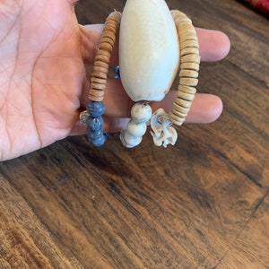 Pu&ograve; includere: Tre braccialetti di perline con un ciondolo a forma di conchiglia bianca. I braccialetti sono fatti di perline marroni, beige e blu.